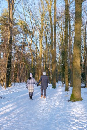 Téléchargez les photos : Un couple d'hommes et de femmes marchant dans la forêt avec de la neige pendant une froide journée d'hiver aux Pays-Bas, au parc national Sallandse Heuvelrug - en image libre de droit