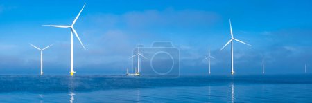 Photo for Aerial view at Windmill park with fishing boat and windmills turbines during winter , generating electricity with a blue sky green energy concept at Urk Netherlands - Royalty Free Image