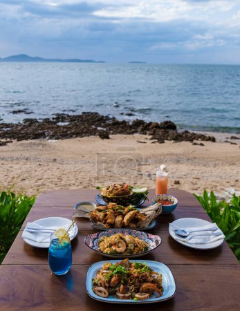 Photo for Dinner table with Thai food and bbq fish on the beach of Pattaya Thailand. - Royalty Free Image
