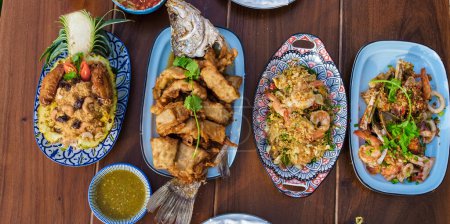Téléchargez les photos : Table à manger avec de la nourriture thaïlandaise et du poisson barbecue sur la plage de Pattaya Thaïlande pendant le coucher du soleil - en image libre de droit