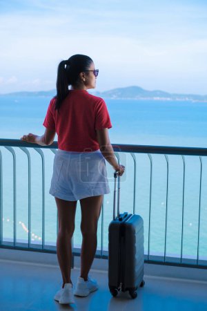 Photo for A women with hand luggage and a trolley checking in at a hotel room looking out over the ocean in Thailand. - Royalty Free Image