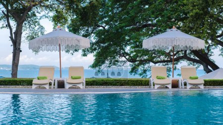 Téléchargez les photos : Chaises longues dans une piscine avec parasols, chaise longue dans une piscine le matin - en image libre de droit