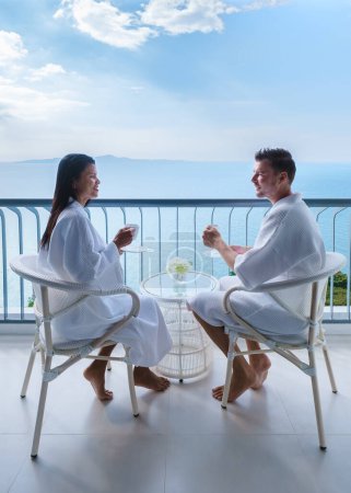 Téléchargez les photos : Les femmes asiatiques et les hommes caucasiens boivent du café dans un hôtel sur le balcon donnant sur l'océan en Thaïlande - en image libre de droit