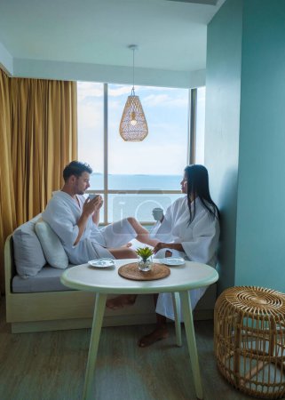 Foto de Mujeres asiáticas y hombres caucásicos toman café en un hotel en el balcón con vistas al océano en Tailandia - Imagen libre de derechos