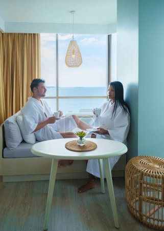 Foto de Un par de mujeres asiáticas y hombres caucásicos toman café en un dormitorio de hotel con vistas al océano en Tailandia - Imagen libre de derechos