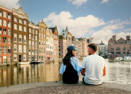 Photo for Amsterdam Damrak during sunset, happy couple man and woman during sunset at the canals, a dutch couple at Waterfront by Dancing house of Amsterdam on a city trip - Royalty Free Image