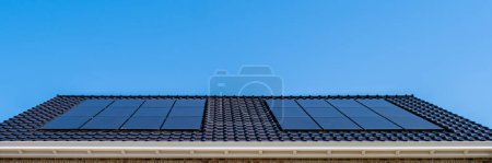 Foto de Casas de nueva construcción con paneles solares negros unidos al techo contra un cielo azul soleado en los Países Bajos. Energía solar procedente de paneles solares - Imagen libre de derechos
