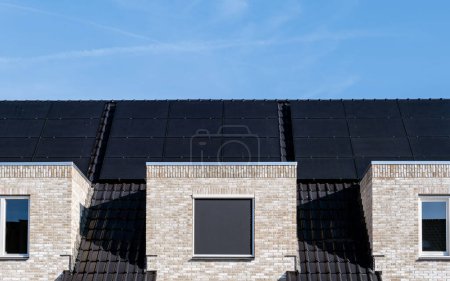 Photo for Newly build houses with black solar panels attached to the roof against a sunny blue sky in the Netherlands. Sun energy from solar panels - Royalty Free Image