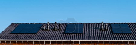 Foto de Casa con paneles solares negros unidos al techo contra un cielo azul soleado en los Países Bajos. Energía solar procedente de paneles solares - Imagen libre de derechos