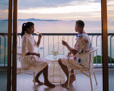 Téléchargez les photos : Quelques hommes caucasiens et femmes thaïlandaises boivent des cocktails sur le balcon d'un hôtel à Pattaya Thaïlande au coucher du soleil. - en image libre de droit