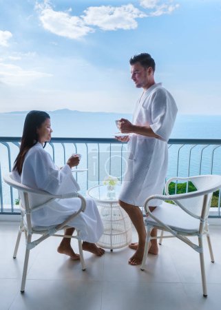 Téléchargez les photos : Quelques femmes asiatiques et des hommes caucasiens boivent du café dans un hôtel sur le balcon donnant sur l'océan en Thaïlande - en image libre de droit