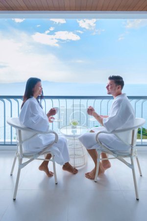 Foto de Un par de mujeres asiáticas y hombres caucásicos toman café en un hotel en el balcón con vistas al océano en Tailandia - Imagen libre de derechos