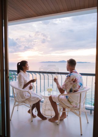 Téléchargez les photos : Quelques hommes caucasiens et femmes thaïlandaises boivent des cocktails sur le balcon d'un hôtel à Pattaya Thaïlande au coucher du soleil. - en image libre de droit