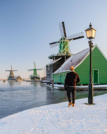 Foto de Jóvenes visitan el pueblo molino de viento de Zaanse Schans durante el invierno con paisaje de nieve en el pueblo holandés de Holanda en invierno - Imagen libre de derechos