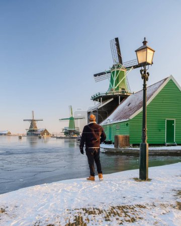Téléchargez les photos : Village du moulin à vent de Zaanse Schans en hiver avec des jeunes hommes regardant la maison historique aux Pays-Bas - en image libre de droit