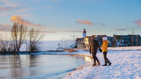Téléchargez les photos : Phare d'Urk en hiver avec paysage enneigé aux Pays-Bas. Femmes asiatiques et hommes caucasiens visitant Urk pendant l'hiver en Hollande - en image libre de droit