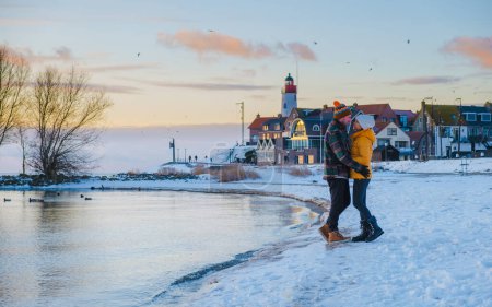 Téléchargez les photos : Phare d'Urk en hiver avec paysage enneigé aux Pays-Bas. Un couple de femmes asiatiques et hommes caucasiens visitant Urk pendant l'hiver en Hollande - en image libre de droit