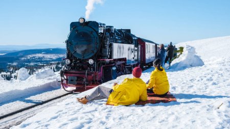 Téléchargez les photos : Couple d'hommes et de femmes regardant le train à vapeur pendant l'hiver dans la neige dans le parc national du Harz Allemagne, train à vapeur sur le chemin de Brocken à travers le paysage hivernal, Brocken, Harz Allemagne - en image libre de droit