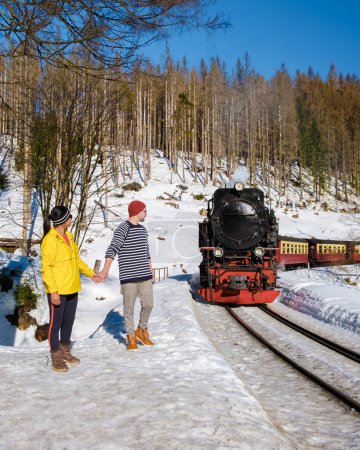 Foto de Un par de hombres y mujeres caminando por el tren de vapor durante el invierno en la nieve en el parque nacional de Harz Alemania, tren de vapor Brocken Bahn en el camino a través del paisaje de invierno, Brocken, Harz - Imagen libre de derechos