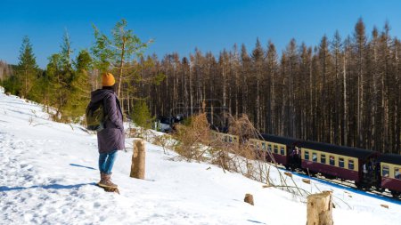 Téléchargez les photos : Femmes regardant le train à vapeur pendant l'hiver dans la neige dans le parc national du Harz Allemagne, train à vapeur Brocken Bahn sur le chemin à travers le paysage hivernal, Brocken, Harz Allemagne - en image libre de droit