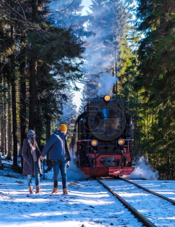 Foto de Un par de hombres y mujeres caminando frente a un tren de vapor durante el invierno en la nieve en el parque nacional de Harz Alemania, tren de vapor Brocken Bahn - Imagen libre de derechos