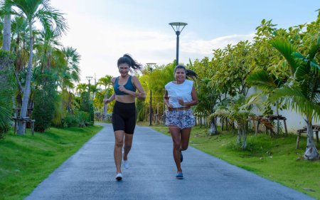Téléchargez les photos : Deux femmes asiatiques font de l'exercice dans un parc public à Pattaya en Thaïlande. Des amies font du jogging. Femme mûre thaïlandaise exercice dans un parc avec des palmiers dans la ville Pattaya - en image libre de droit