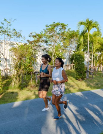 Téléchargez les photos : Deux femmes asiatiques font de l'exercice dans un parc public à Pattaya en Thaïlande. Des amies font du jogging. Thai femme mûre exercice dans un parc avec des palmiers - en image libre de droit