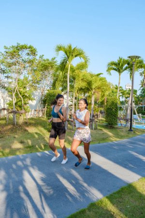 Photo for Two Asian women exercise running in a public park in Pattaya Thailand. Female friends jogging. Thai mature woman exercise in a park with palm trees in the city - Royalty Free Image