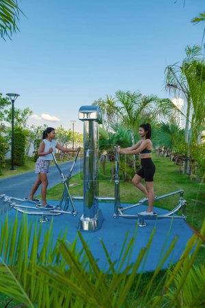 Téléchargez les photos : Deux femmes asiatiques séance d'entraînement fitness dans un parc public à Pattaya Thaïlande. Femme mûre thaïlandaise exercice dans un parc avec des palmiers dans la ville - en image libre de droit