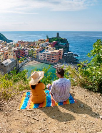 Foto de Un par de hombres caucásicos y mujeres asiáticas están en la colina con vistas a la bahía de Vernazza pueblo Cinque Terre Parque Nacional Italia, El pintoresco pueblo costero de Vernazza en un día soleado - Imagen libre de derechos