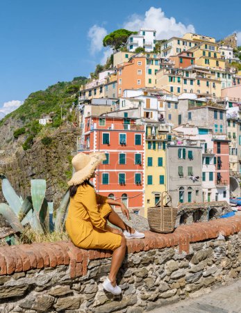 Téléchargez les photos : Femmes asiatiques avec un chapeau visiter Riomaggiore Cinque Terre magnifique vue sur la Ligurie, Italie. paysage marin de la mer Méditerranée. Concept de voyage arrière-plan. - en image libre de droit