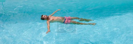 Téléchargez les photos : Jeunes hommes caucasiens flottant dans une piscine bleue pendant l'été. - en image libre de droit