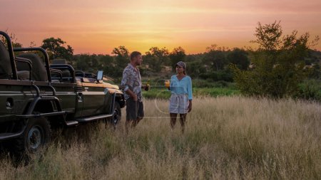 Téléchargez les photos : Femmes asiatiques et hommes européens en safari dans le parc national Kruger en Afrique du Sud. Deux hommes et deux femmes en safari. Touristes dans une jeep à la recherche coucher de soleil avec des boissons sur safari - en image libre de droit