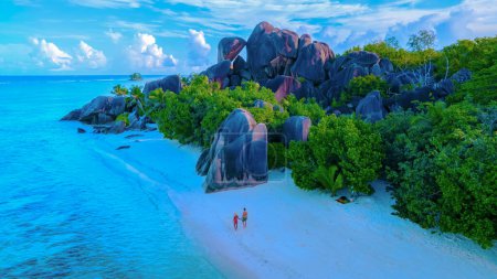 Téléchargez les photos : Anse Source dArgent beach, La Digue Island, Seychelles, vue. de l'île tropicale, couple d'hommes et de femmes marchant sur la plage pendant le coucher du soleil lors de vacances de luxe aux Seychelles - en image libre de droit