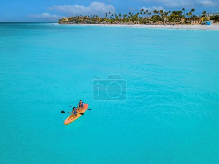 Photo for Couple Kayaking in the Ocean on Vacation Aruba Caribbean sea, man and woman mid age kayak in ocean blue clear water with white beach and palm trees Aruba - Royalty Free Image