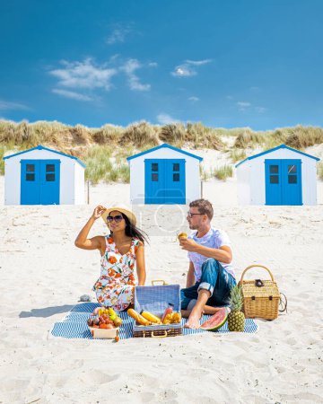 Téléchargez les photos : Pique-nique sur la plage Texel Pays-Bas, couple ayant un pique-nique sur la côte de Texel avec du sable blanc et une withe colorée et maison bleue en Hollande - en image libre de droit