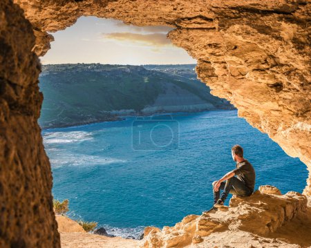 Téléchargez les photos : Gozo île de Malte, un jeune homme dans une grotte donnant sur l'océan et une vue sur la baie de Ramla, de l'intérieur Tal Mixta Grotte Gozo Europe - en image libre de droit
