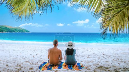 Téléchargez les photos : Plage de sable blanc tropicale à Praslin île de Seychelles, heureux Jeune couple homme et femme pendant les vacances Vacances à la plage se détendre sous un palmier - en image libre de droit
