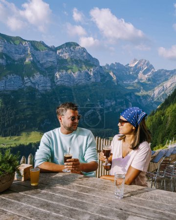 Foto de Pareja tomando café en un restaurante en los Alpes suizos, restaurante de montaña bajo el acantilado de Aescher visto desde la montaña Ebenalp en la región de Appenzell en Suiza Acantilado de Aescher Suiza, - Imagen libre de derechos