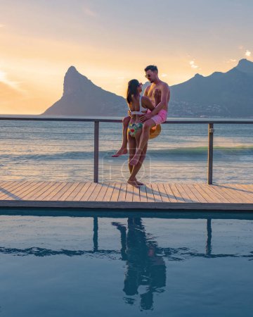 Photo for Couple man and women in front of Infinity pool looking out over the ocean of Cape Town South Africa, man and woman in a swimming pool during sunset. - Royalty Free Image