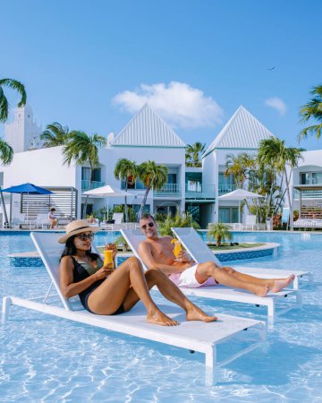 Foto de Resort de lujo con piscina cerca de Palm Beach Aruba Caribe, pareja de hombres y mujeres de mediana edad en unas vacaciones de lujo en el Caribe bebiendo cócteles, pareja de vacaciones - Imagen libre de derechos