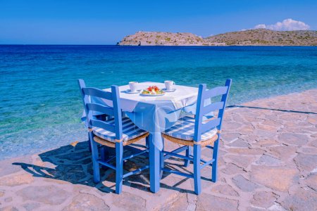 Foto de Creta Grecia Plaka Lassithi con su tradicional mesa azul y sillas y la playa de Creta Grecia. Paralia Plakas, pueblo de Plaka Creta - Imagen libre de derechos
