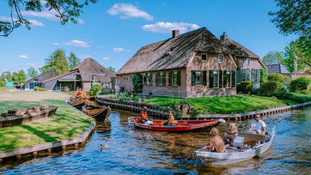 GIETHOORN, NETHERLANDS May 2020 typical houses and tourists in colorful electric boats in Giethoorn, The Netherlands. The beautiful houses and gardening city is known as Venice of the North in Europe