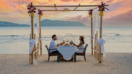 Téléchargez les photos : Dîner romantique sur la plage à Phuket en Thaïlande, couple homme et femme d'âge moyen femme asiatique et homme européen dînant sur la plage en Thaïlande pendant le coucher du soleil. - en image libre de droit