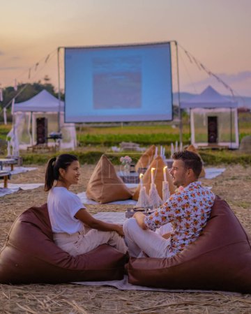 Téléchargez les photos : Les gens qui regardent des films dans les cinémas en plein air la nuit dans la campagne du nord de la Thaïlande., film en plein air, les couples qui regardent des films à l'extérieur sur un écran - en image libre de droit