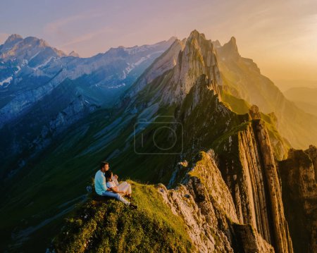 Foto de Pareja observando la puesta de sol en el borde de una montaña en Suiza durante las vacaciones de verano, Schaeffler Altenalptuerme montaña cresta Appenzell Innerrhoden Suiza - Imagen libre de derechos