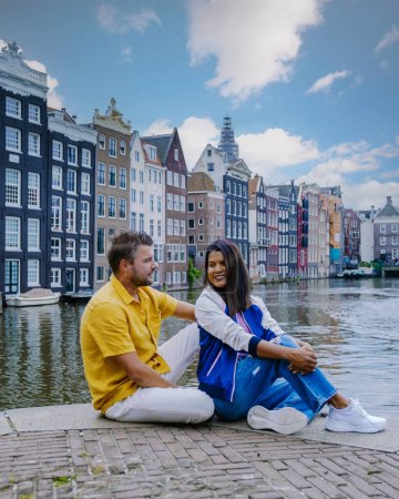 Photo for Amsterdam Netherlands, happy couple man and woman on a summer evening at the canals of Amsterdam. Man and woman mid age Asian girl and European men on a city trip in Amsterdam Netherlands - Royalty Free Image