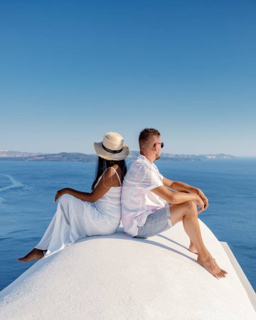 Téléchargez les photos : Un couple en vacances à Santorin en Grèce, deux hommes et femmes visitent Oia Santorin avec des bâtiments blanchis à la chaux. à Santorin Grèce - en image libre de droit
