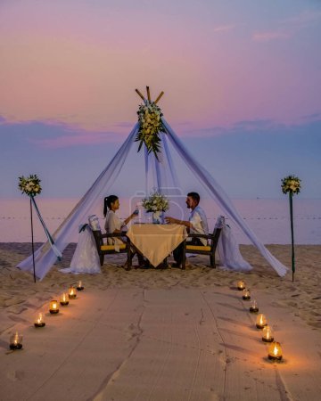 Foto de Cena romántica en la playa de Phuket Tailandia, pareja hombre y mujer de mediana edad mujer asiática y hombre europeo cenando en la playa de Tailandia al atardecer. - Imagen libre de derechos