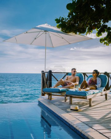 Téléchargez les photos : Curaçao, couple homme et femme d'âge moyen se relaxant au bord de la piscine pendant les vacances, hommes et filles au bord de la piscine à Curaçao pendant les vacances sur une île tropicale vacances de luxe - en image libre de droit